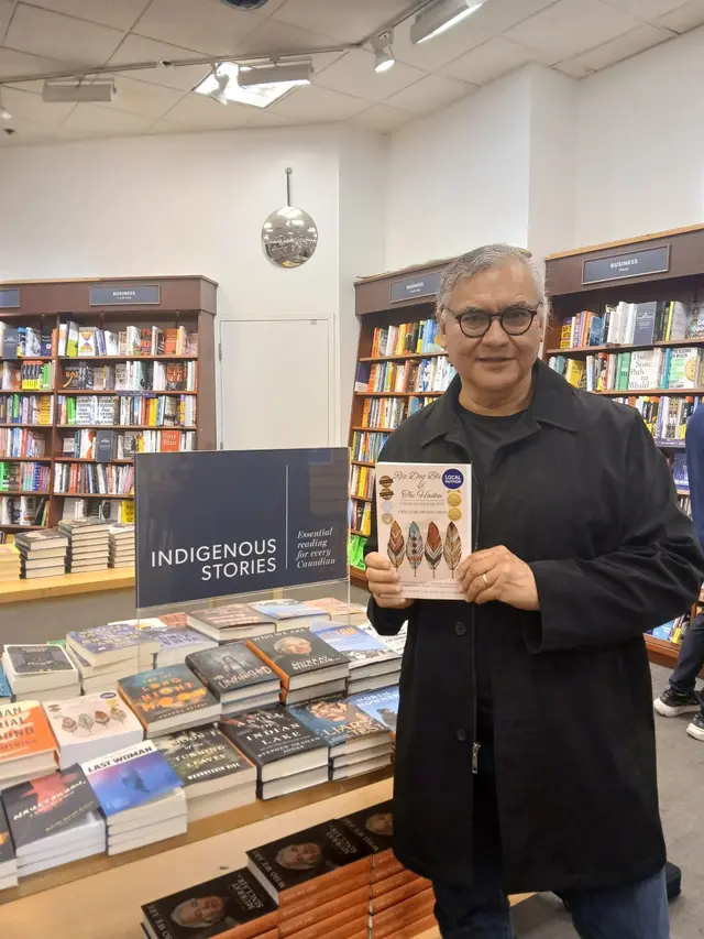 William holding his book beside an Indigenous Stories display in a bookstore