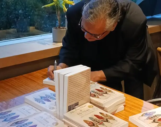 William signing a copy of the book at a table stacked with copies